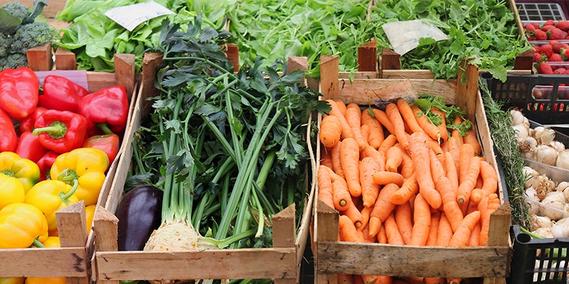 Eine Holzkiste mit roten und gelben Paprikas, eine weitere mit Sellerieknollen und eine mit Karotten gefüllte Kiste.