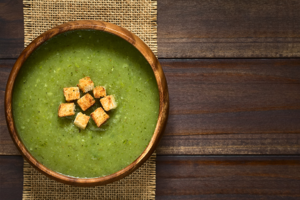 Eine grüne Zucchinisuppe mit Croûtons in einer Holzschüssel.