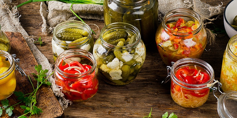 Mehrere Einmachgläser mit Essiggurken, Paprika und Kraut.