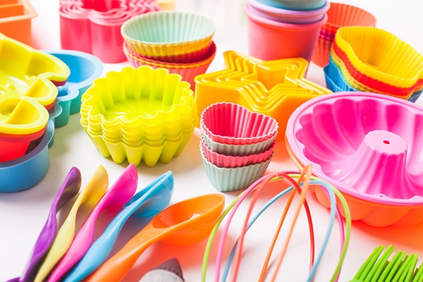 Viele bunte Silikonformen für Muffins, Kuchen oder Kekse. Im Vordergrund liegen bunte Messlöffel und ein Schneebesen.