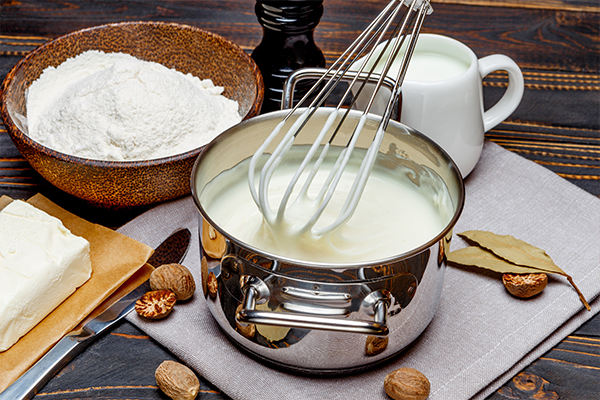 Ein Topf mit Bechamelsoße, die mit einem Schneebesen verrührt wird.