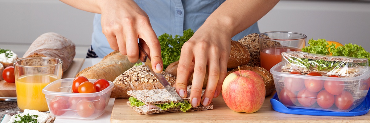 Eine Frau schneidet ein belegtes Knäckebrot in zwei Hälften. Daneben sind Aufbewahrungsdosen gefüllt mit Cocktailtomaten.