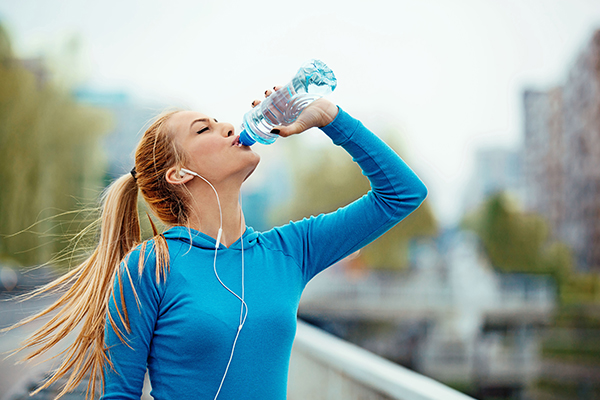Eine Joggerin im blauen Kapuzenpulli trinkt aus ihrer Wasserflasche