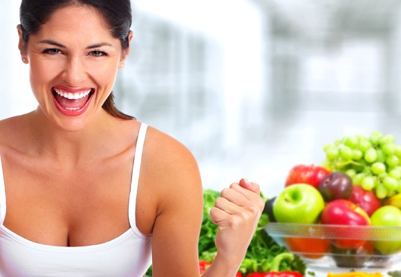 Eine Frau in weißem Trägershirt ballt motiviert die Fäuste. Im Hintergrund ist eine Schüssel mit Obst.