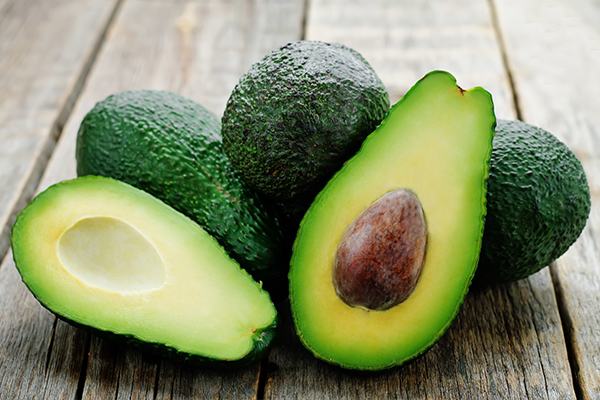 Vier Avocados auf einer Holzfläche. Eine Frucht ist in zwei Hälften geteilt.
