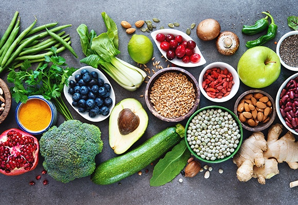 Ein aufgeschnittener Granatapfel, eine Schüssel mit Heidelbeeren, eine halbe Avocado und mehrere Schüsseln mit Linsen, Goji-Beeren und Mandeln.