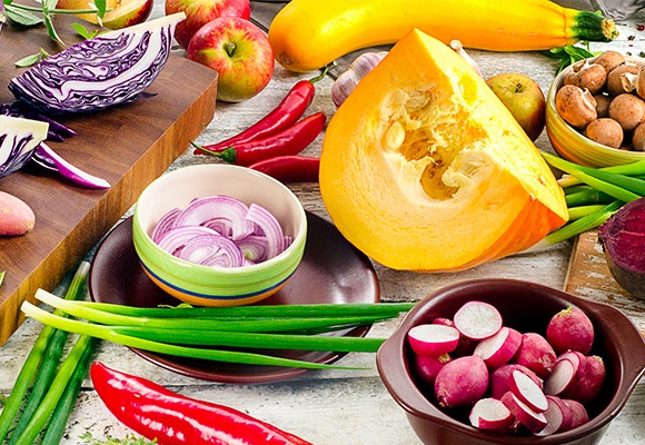 Aufgeschnitte Zwiebel und Radieschen in Schüsseln. Daneben ein aufgeschnittener Kürbis.