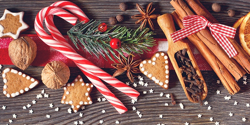 Weihnachtliche Dekorationen auf einem Tisch: Plätzchen, Zimt, Orangenscheiben, Nüsse, Zuckerstangen und Tannenzweige.