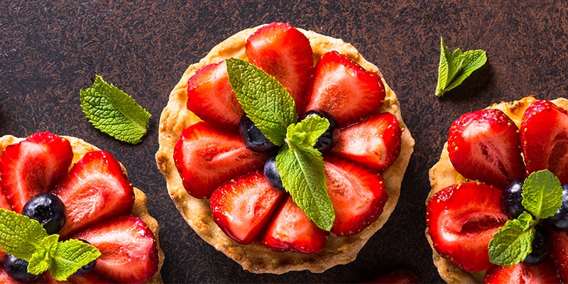 Drei Erdbeertarts mit Minzblättern und Heidelbeeren garniert.