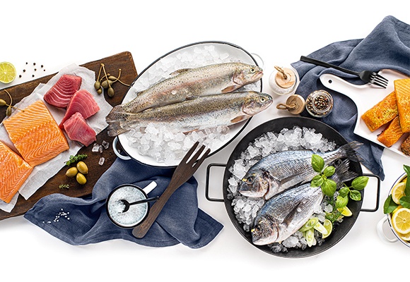 Aufgeschnittener Frisch wie Lachs und Thunfisch liegen auf einem Holzschneidebrett. Ganzer Fisch liegt gekühlt auf Eiswürfeln. Zitronen und Gewürze runden das Bild ab.