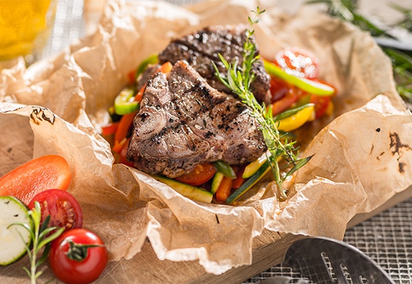 Saftig-zartes Fleisch liegt auf buntem Gemüse und wurde mediterran zubereitet.