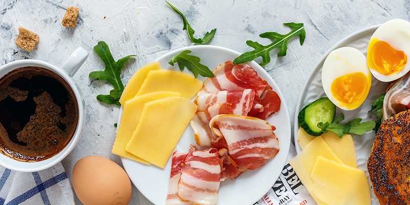 Buntes Frühstück mit Kaffee, Käse, Wurst, Ei und Mohnbrötchen steht auf rustikalem Holzuntergrund.
