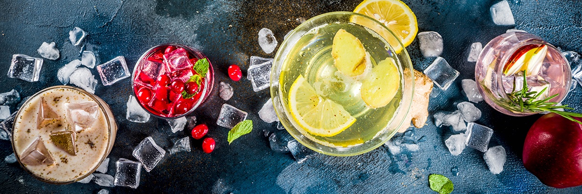 Vier bunte Getränke werden von oben gezeigt, um sie herum liegen Eiswürfel. Sie sind mit verschiedenen Früchten wie Zitronen und Cranberrys gefüllt.