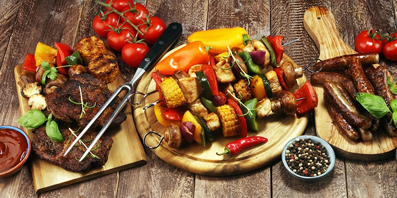 Grillspieße, Steaks und Würstchen liegen auf Holzbrettchen.