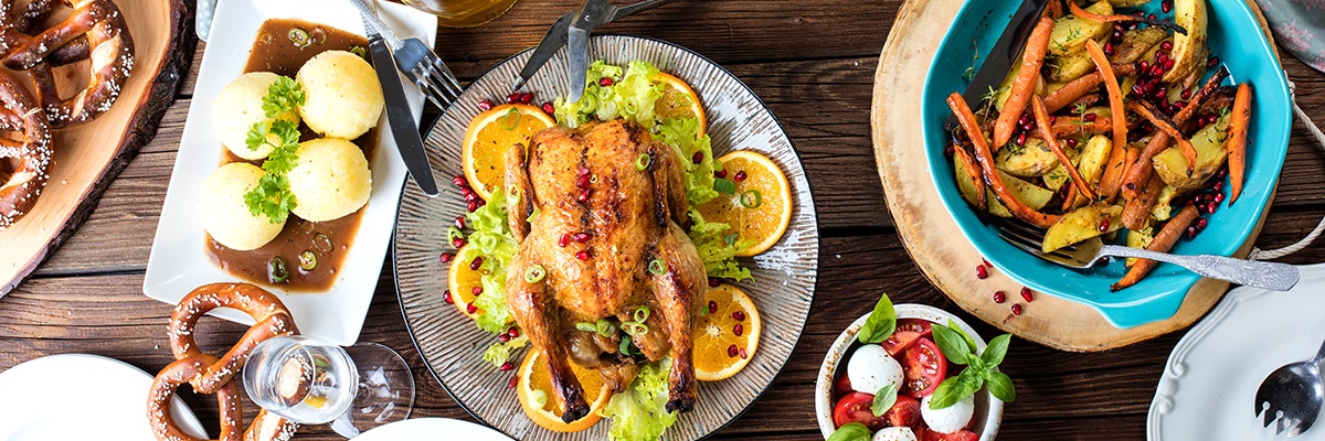 Ein Teller mit einer gebratenen Ente, daneben ein blauer Teller mit Gemüse. Auf einem Teller links sind vier Knödel mit brauner Soße.