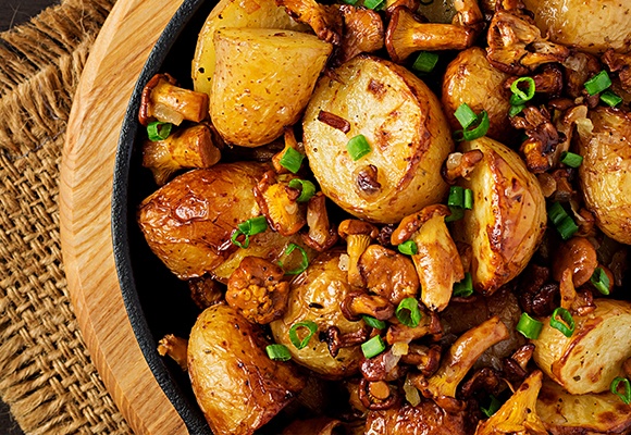 Gebratene Kartoffeln mit Frühlingszwiebeln und Pilzen liegen in einer Pfanne.
