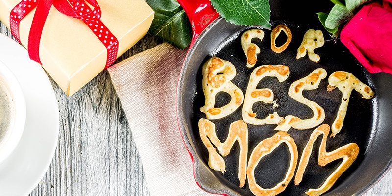 Ein Tisch gedeckt für den Muttertag mit Rosen, Kaffee und Teig der "For best mom" zeigt.