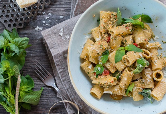 Klassische Pasta ohne Soße mit Gewürzen liegt auf einem hellblauen Teller, links davon Kräuter.