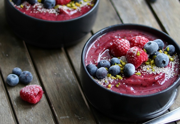 Ein Obstsmoothie ist mit gefrorenen Himbeeren und Heidelbeeren drapiert.