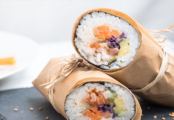 Maki Sushi: Klebereis ist eingerollt in einem Noriblatt und Papier. Es liegt auf einer Steinplatte.