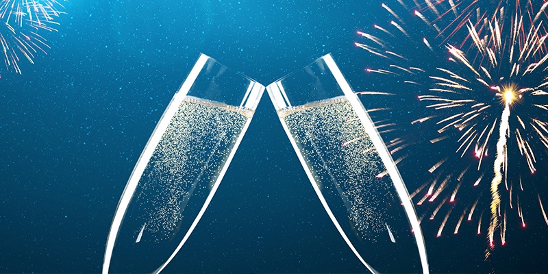 Zwei gefüllte Sektgläser stoßen bei Feuerwerk in der Nacht an.