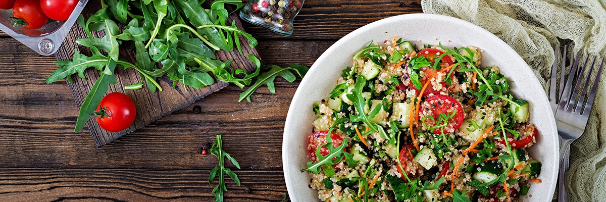 Ein bunter Salat mit Rucola, Tomaten, Gurke und Couscous neben zwei Gabeln.