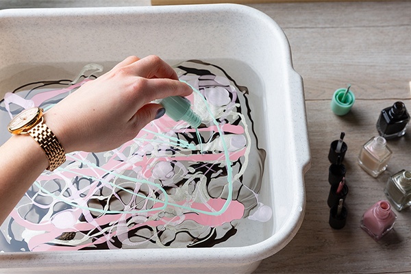 Nagellack in verschiedenen Farben in eine Schüssel mit Wasser geben