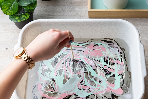 Die Nagellack-Töne im Wasserbecken mit einem Holzstäbchen vermischen