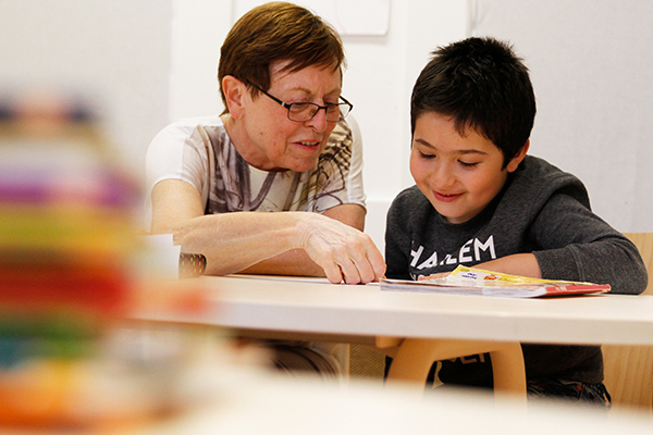 Mann sitzt mit Kind an einem Tisch und hilft bei den Hausaufgaben