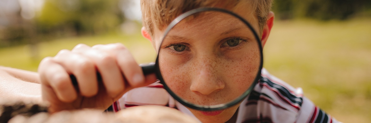 Junge betrachtet etwas durch eine Lupe