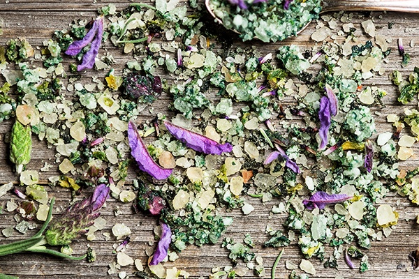 Die bunte Mischung aller Badesalz-Zutaten auf dem Tisch verteilt, neben einem Löffel