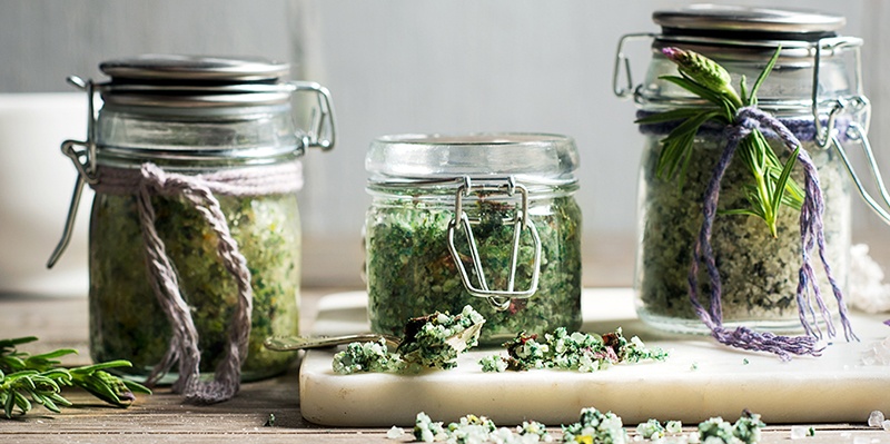 Drei Einweggläser mit Badesalz und Geschenkband verpackt auf einem Tisch mit passender Dekoration