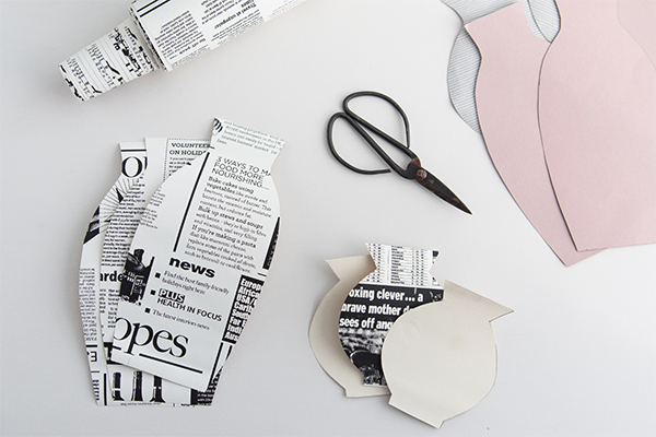 Ausgeschnittene Vasen auf Zeitungspapier und rosa Papier.