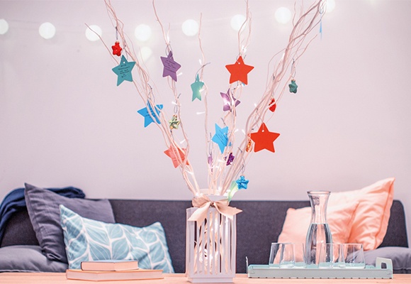 Helle Äste mit Bunten Sternen in einer Vase auf dem Tisch vor einem gemütlichen Sofa