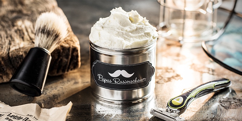 Natürlicher Rasierschaum abgefüllt in einer beschrifteten Dose, daneben Rasierer & Pinsel auf dem Tisch