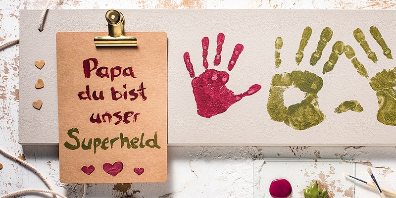 Holzschild mit Aufschrift "Papa du bist unser Superheld" und Handabdrücke