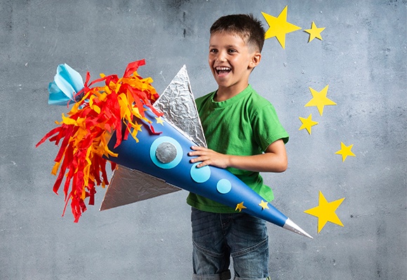 Schultüte mit Dekoration im Weltraum-Stil zum Selberbasteln in der Hand eines aufgeregten Schulkindes 