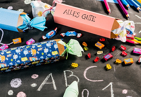 Bunte DIY-Schultüten und Süßigkeiten auf einer beschrifteten Kreidetafel