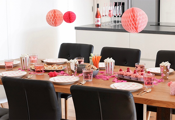 Eine gedeckte Tafel für eine Party mit rosa Deko, Tellern, Cupcakes und Popcorn