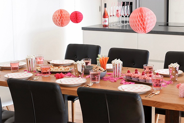 Gedeckter Tisch mit rosa Accessoires, darüber hängen selbstgemachte Papier-Lampions