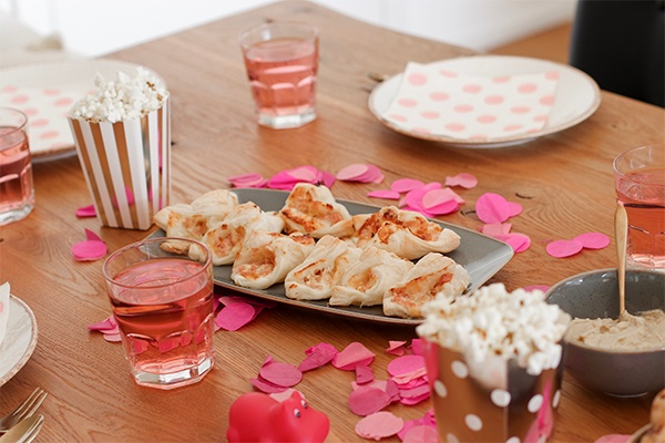 Gebackene Schinken-Käse-Blätterteig-Kipferl auf dem Tisch, daneben Party-Dekoration, Teller und Getränke