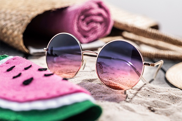 Etuis in melonen-Optik, daneben die Sonnenbrille und Strandtasche im Sand