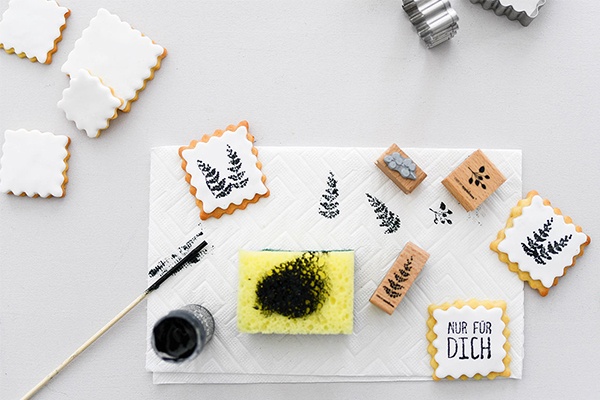 Lebensmittelfarbe, ein Schwamm und Holzformen zum Bedrucken der Kekse