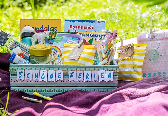Bunte Kiste mit Aufschrift "Schöne Ferien" auf einer Wiese