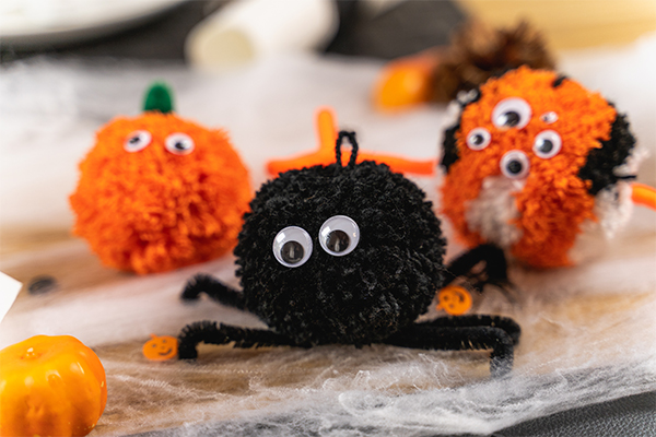 Schwarze Pompoms als Spinne und orange stellen ein Monster und Kürbisse dar