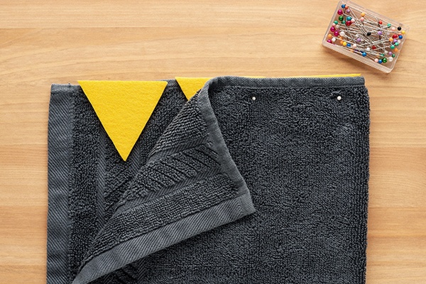 Die gelben Dinozacken werden mit Nadeln an einem grauen Handtuch befestigt