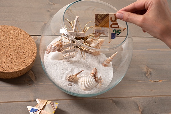 Geldscheine dekorativ im Glas mit Sand platzieren