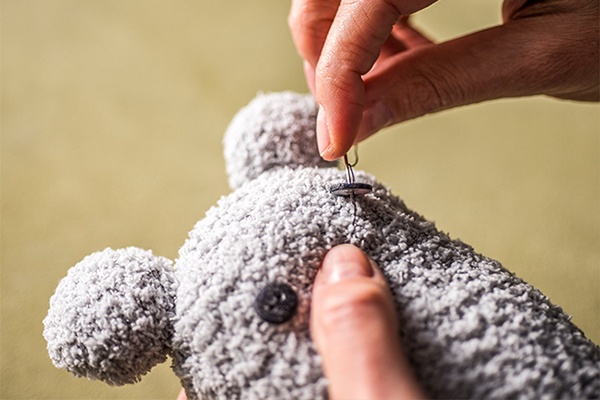 Süßes Gesicht aus Knöpfen auf den Koala-Plüschbären nähen