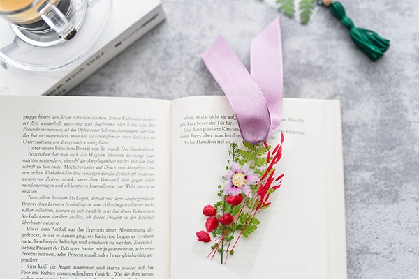 Lesezeichen mit Blüten und Blättern in einem aufgeklappten Buch, daneben eine Tasse Kaffee