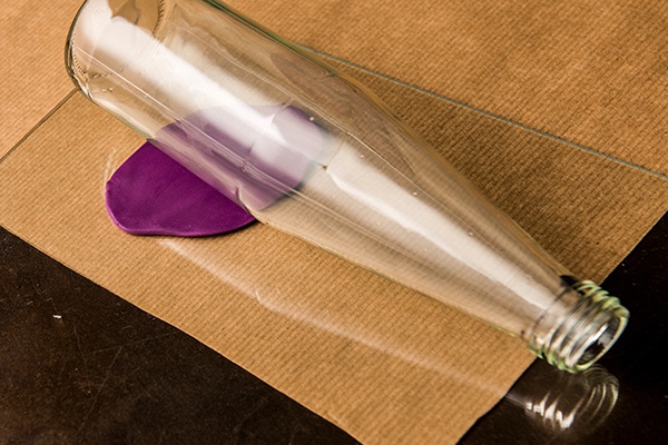 FIMO-Knetmasse mit einer Flasche auf Papier ausrollen